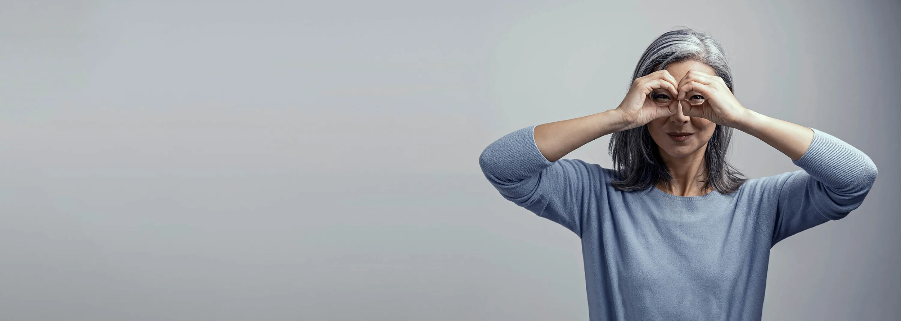 Una donna anziana tiene le mani davanti agli occhi come un binocolo.