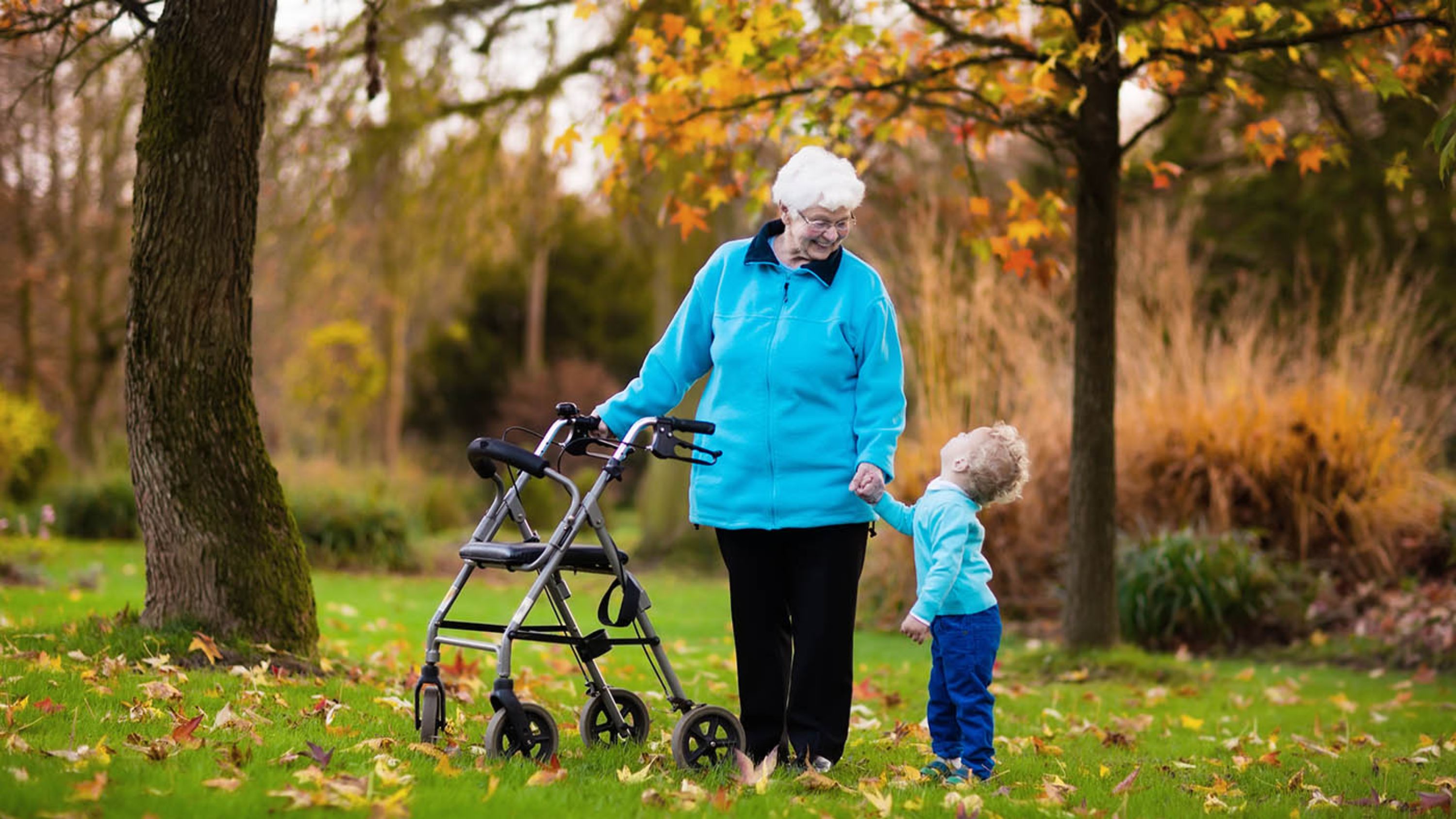 Une dame âgée qui marche avec un déambulateur et tient un enfant dans l'autre main.