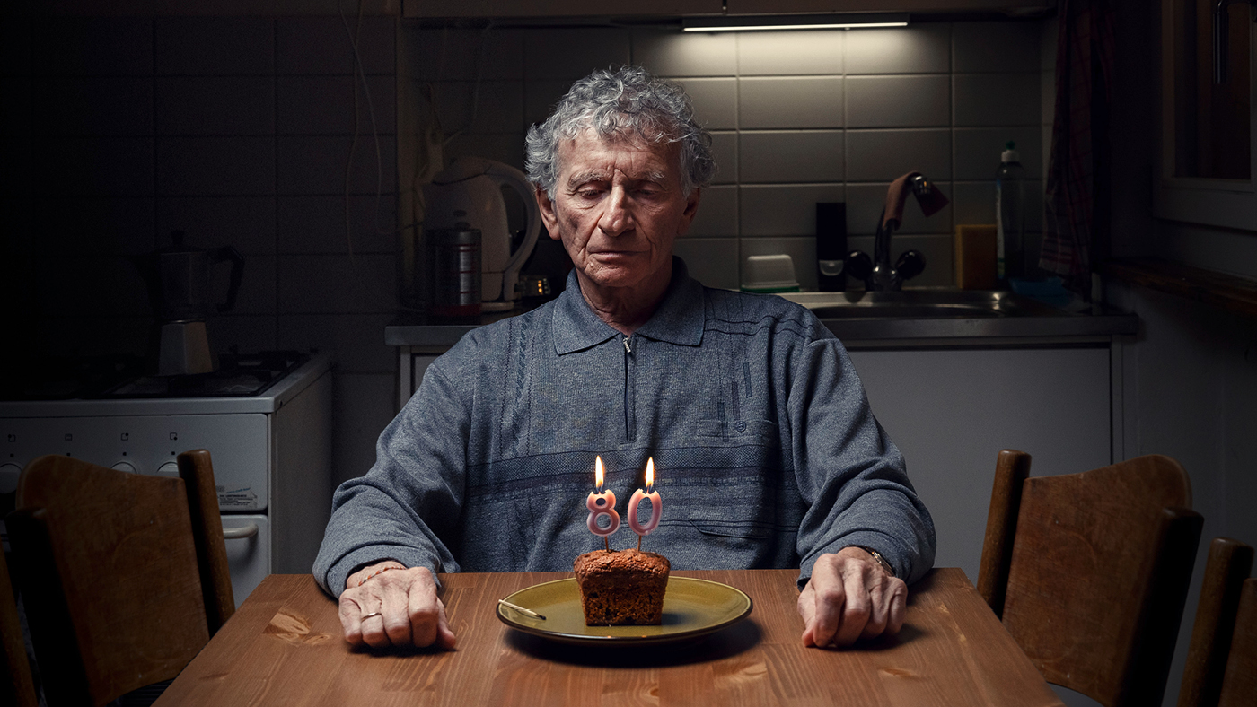 Una persona anziana è seduta da sola davanti a una torta di compleanno.