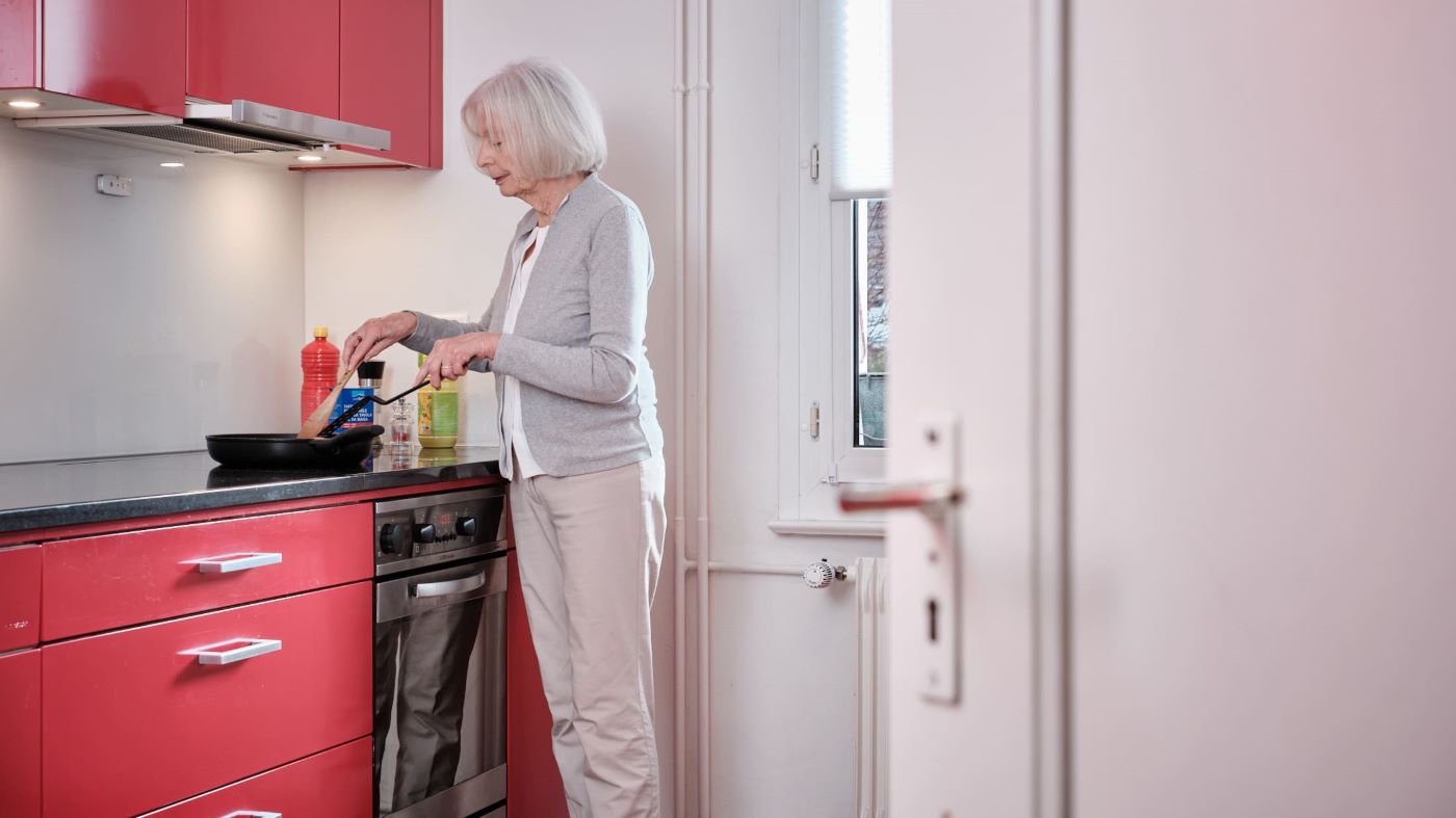 Une femme âgée est dans la cuisine en train de cuisiner